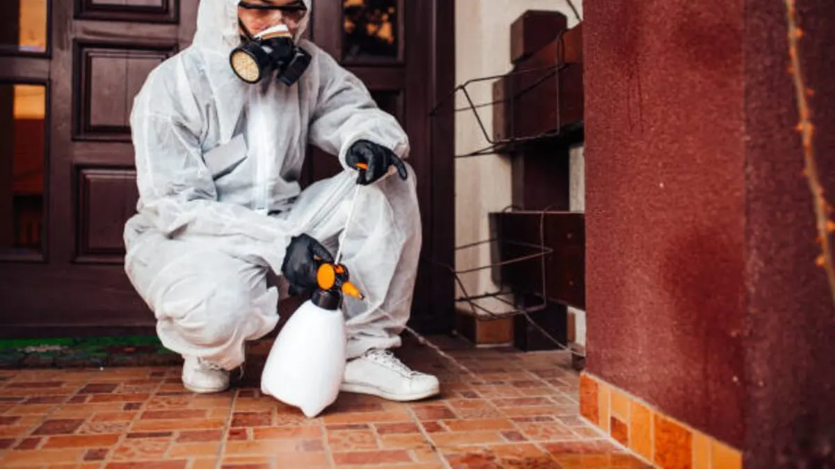 Technician crouching with a sprayer at a front door